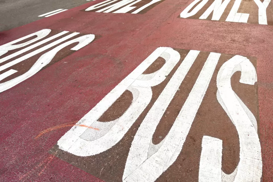 White BUS ONLY letters on red painted bus lane on street.